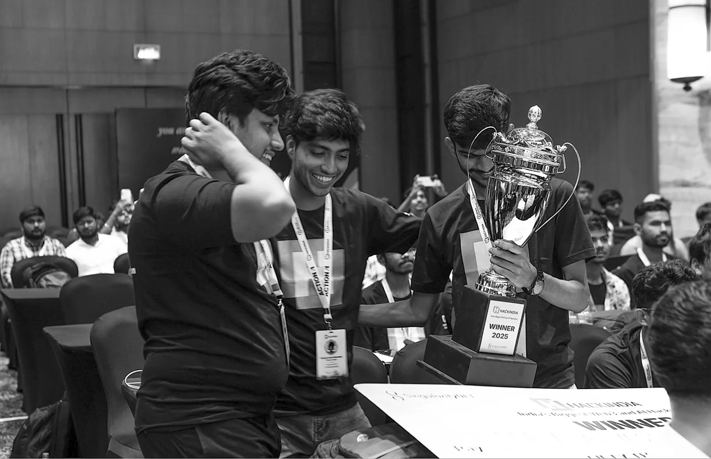 Black-and-white photo of the team admiring the HackIndia 2025 trophy